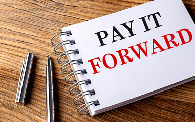 PAY IT FORWARD text on notebook with pen on wooden background