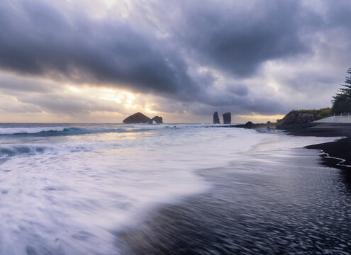 Long exposure of waves on the black sandy beach of Mosteiros with a cloudy sunset and the sea stacks in the background, Mosteiros, Sao Miguel Island, Azores Islands, Portugal, Atlantic