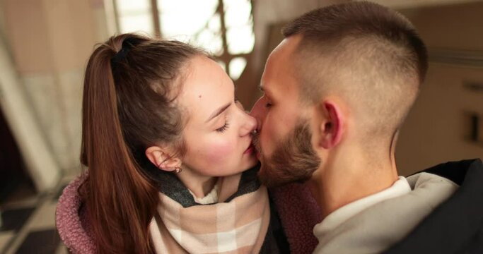 A young couple in love say goodbye with passionate kisses and hugs after a romantic date in the hallway of an apartment building.