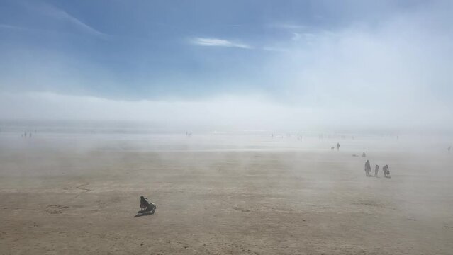 People enjoy walking on foggy sand beach in sunny Tramore, Ireland