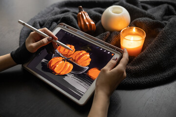 Girl's hands in special glove draw still life picture with pumpkins on electronic tablet near burning candle. The concept of inspiration, creativity, modern art. Halloween, Thanksgiving day