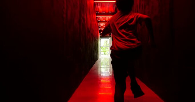 In this intense and heart-pounding scene, young boy is running away from danger through dark corridor with haunting red light overhead. He's fleeing for his life, desperate for freedom