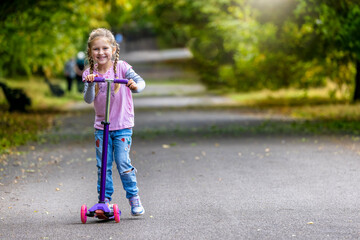 Portrait of a happy, blonde girl enjoying her scooter toy in the public park