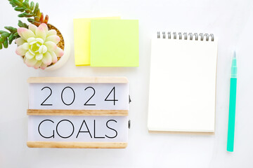 2024 goals on wood box and blank notebook paper on white marble background, business new year aim...