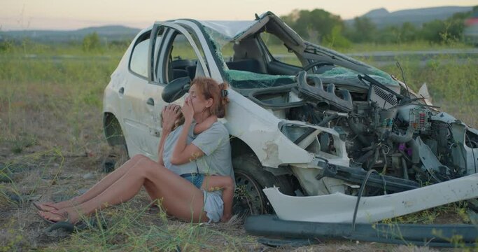 A mother and daughter who survived a car accident stand near a broken car and are glad that they are alive. Life value concept