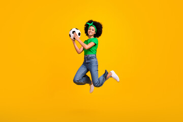 Fototapeta na wymiar Full length photo of sportive excited teenager schoolgirl jump hands hold catch football isolated on yellow color background