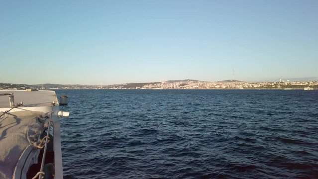 Evening, cinematic slow-mo, a stunning view of Istanbul's Asian continent from a ferry on the Bosphorus. The shot showcases the 15 July Martyrs Bridge (15 Temmuz Sehitler Koprusu) and Camlica Tower.