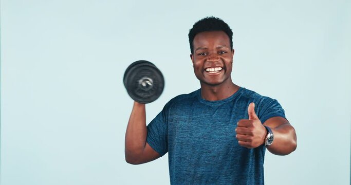Fitness, man and dumbbell with thumbs up for training, exercise or workout in studio on blue background. Weightlifting, person and personal trainer for wellness and healthy body with smile at gym
