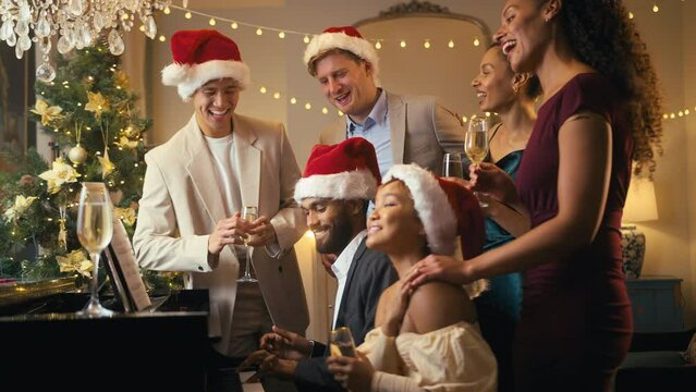 Friends at piano wearing Santa hats and reindeer antlers celebrating at Christmas or new year party - shot in slow motion