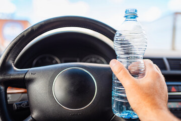 Mans hand holding plastic water bottle inside car while driving a car in traffic.Closeup.