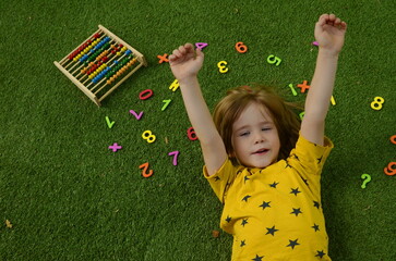 The boy studies the numbers. The child lies on the grass, there are numbers around. Concept:...