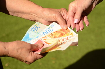 A pensioner woman holds new Israeli shekel banknotes and an Israeli citizen passport in her hands....