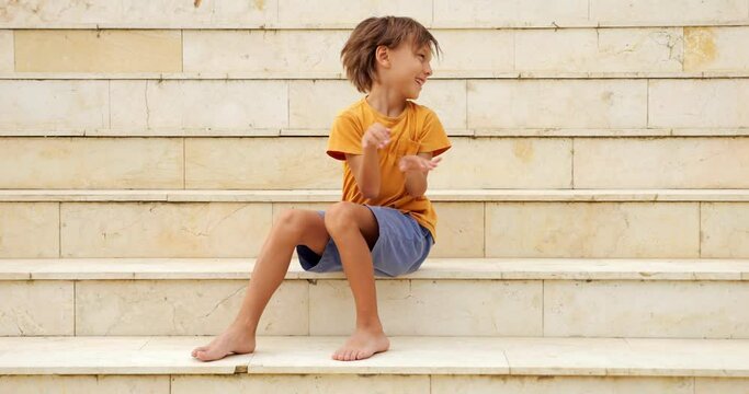 Young boy sits on stairs, filled with joy and laughter. He enthusiastically waves his arms and body, showcasing his playful nature. Delightful portrait of lively and expressive grimacing son