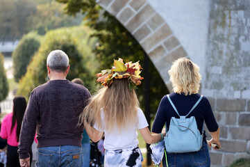 Adult couple with daughter walking in autumn park. Bouquet of maple leaves on the girl head