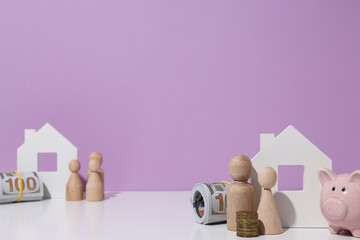 Wooden houses, money, piggy bank and wooden figures on purple background, space for text