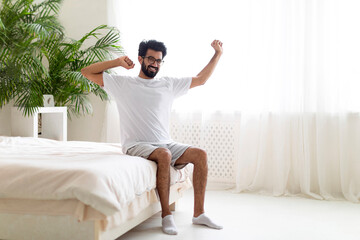 Good Rest. Happy Young Indian Man Stretching Muscles While Sitting On Bed