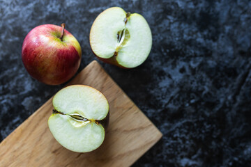 Red apples, cut into halves and slices, lie on a wooden cutting board and a dark background. Apple slices on a marble table close-up. Fruits on a gray background