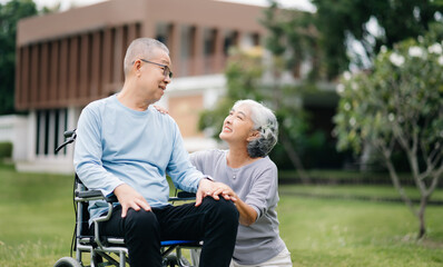 Naklejka premium Asian Senior couple sitting in wheelchairs taking care of each other.in romantic time They laughing and smiling while sitting outdoor in park...