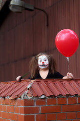 Serious girl in spooky outfit stylized as Pennywise looking at camera while standing in abandoned...
