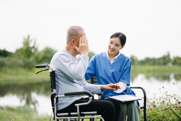 Elderly asian senior man on wheelchair with Asian careful caregiver and encourage patient, walking in garden. with care from a caregiver and senior health insurance..