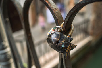 The castle in the form of a fish hangs on the fence of the bridge.