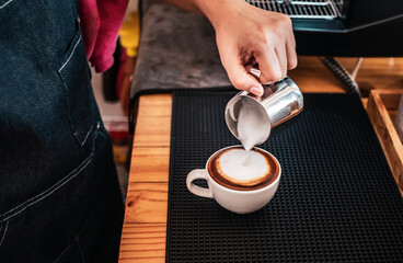 Hand of a barista pouring milk into coffee making cappuccino. Professional barista preparing coffee on the counter.