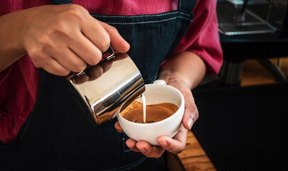 Barista pouring milk into coffee making a cappuccino. Barista making cappuccino,Professional...