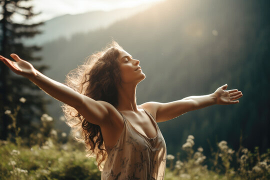 Young beautiful woman with long wavy hair feeling calm and relieved in nature, breathing the fresh air with opened arms