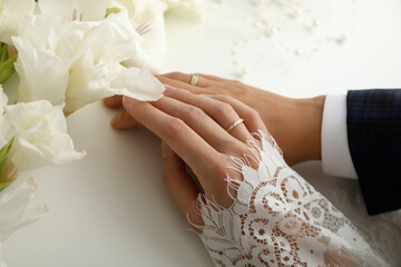 Golden wedding rings on the hands of the newlyweds, on a light background.