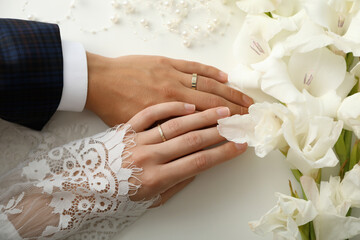Golden wedding rings on the hands of the newlyweds, on a light background.