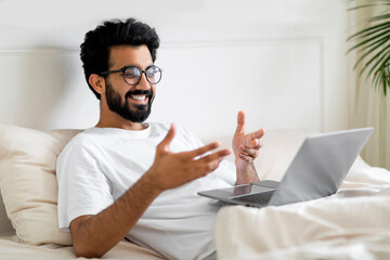 Video Call. Indian Man Making Teleconference Via Laptop While Relaxing In Bed