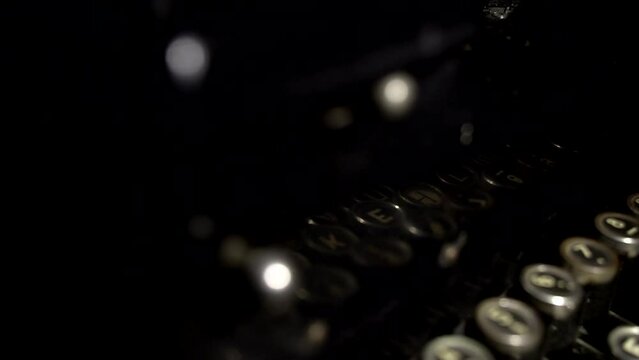 The man is typing on a retro typewriter in dark room. Close up. Fingers strike on buttons
