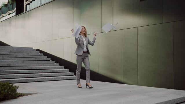 Happy business woman throwing up documents outdoors