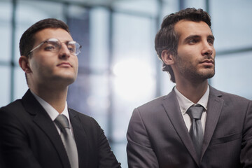 Two serious young businessmen standing with arms crossed in office