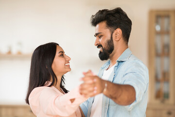 Happy loving indian couple dancing waltz, holding hands, having fun together at home on weekend, side view