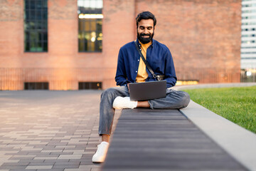 Happy Indian Freelancer Man Using Laptop Computer In Urban Area