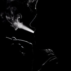 Black and White Silhouette Art Portrait of a Sexy Mysterious Beautiful Female Woman Standing Against the Lights in a Dark Room Hand Holding Smoking a Cigarette. Retro Style Dark Smoke Portrait Shadow