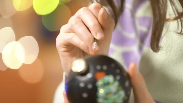 A girl painting Christmas decorations on Christmas eve, prepares for the celebration and decorates the Christmas tree