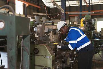 Male engineer worker working with lathe machine in industry factory, wearing safety uniform, helmet. Male technician worker maintenance parts of machine in workshop plant