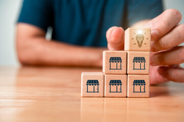 Store franchise expansion for increase sales volume on wooden table. Man hold block cube lightbulb...