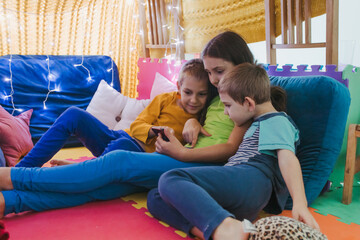 Children play with smartphone at home lying on pillows under the covered blanket - 653258818