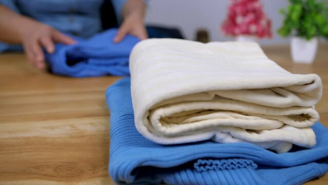 Closeup shot of organizing the clothes at home - Household work concept   cupboard sorting. Indian female folding the clothes on the table - Arranging the stack of clothes from the closet  Organisi...