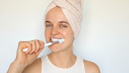 Oral hygiene and dental care. Healthy teeth and gums. Charming optimistic woman wrapped in towel on her head brushing teeth with toothbrush isolated over white background.