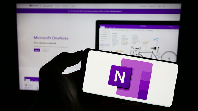 Stuttgart, Germany - 09-21-2023: Person holding mobile phone with logo of note-taking software Microsoft OneNote on screen in front of business web page. Focus on phone display.