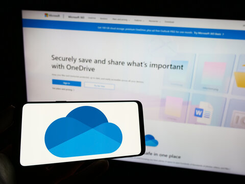 Stuttgart, Germany - 09-21-2023: Person holding cellphone with logo of file hosting service Microsoft OneDrive on screen in front of business webpage. Focus on phone display.
