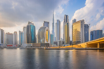 Sunset in Dubai. Skyscrapers and Burj Khalifa in the evening. Skyline with cloudy sky and waterfront in Dubai port. Houses with glass front and concrete facades architecture - obrazy, fototapety, plakaty