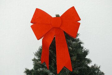 Stylish christmas fir tree with red bow on top against white wall at house entrance. Modern minimal...