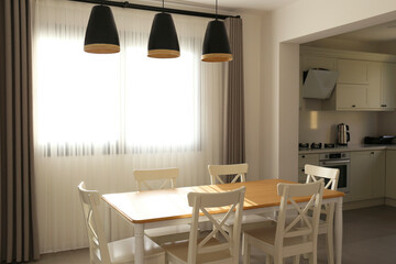 Stylish open plan kitchen with pendant light fixtures, empty dining table and a big window. Copy space, background.