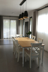 Stylish dining room with pendant light fixtures, empty table and a big full length windows. Copy space, background.