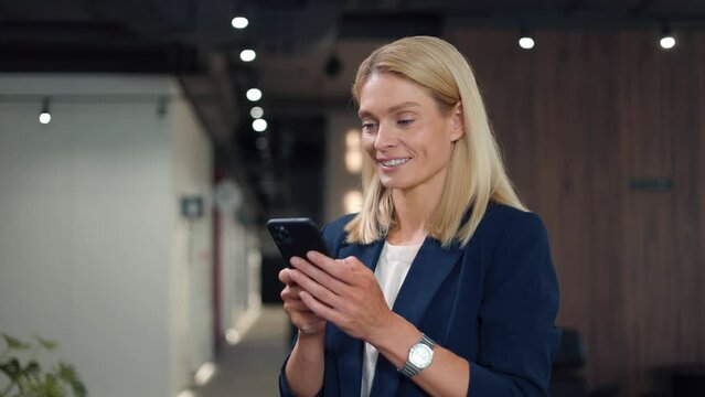 Charming woman texting with colleagues at work on personal smartphone. Smiling caucasian businesswoman using modern technology to keeping in touch with important people. Concept of communication.